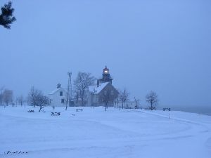 The lighthouse is lit up as the snow comes down.