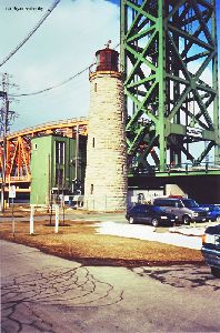 The lighthouse tower is dwarfed by the bridge.