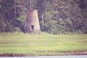 Lighthouse on a grassy ledge overlooking the river.